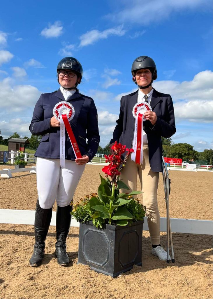 two horse riders standing with rosettes
